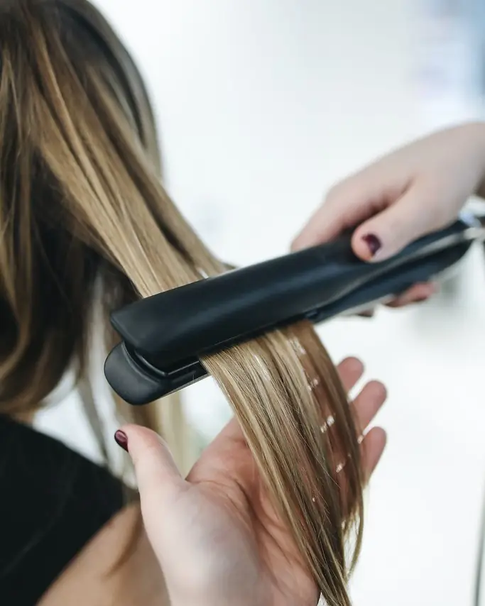 A hairdresser straightening long blonde hair with a pair of hair straighteners